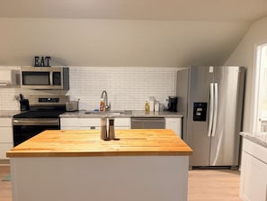 Cozinha moderna com ilha de madeira, eletrodomésticos de aço inoxidável e painel de parede em tijolos brancos.