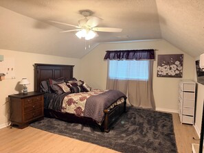 A bedroom with a bed, a ceiling fan, a window with curtains, a dresser, and a wall-mounted lamp. - Furnished Apartment l League City l Business & Medical Travelers (Dickinson)