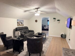 A living room with a ceiling fan, a sofa, a coffee table, and a television. - Furnished Apartment l League City l Business & Medical Travelers (Dickinson)