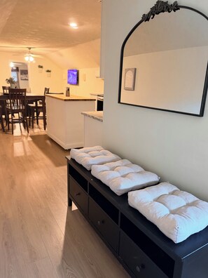Ett hotellrum med trägolv, en svart bänk med vita kuddar, en väggmonterad spegel och en matplats i bakgrunden.