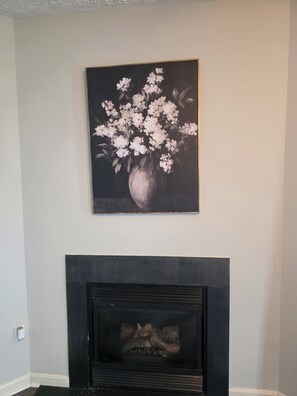 A painting of white flowers in a vase on a wall, a black fireplace below, and a white wall.