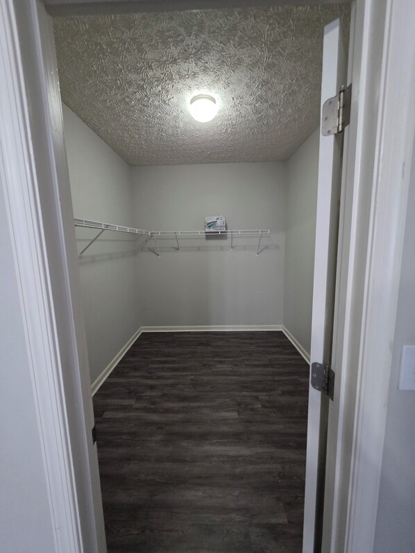 A narrow hallway with a wooden floor, a ceiling light, and a clothes rack with a box on it.