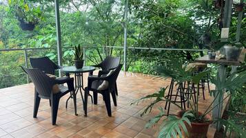 Eine Terrasse im Freien mit Fliesenboden, zwei Korbstühle, einem kleinen runden Tisch und verschiedenen Kübelpflanzen.