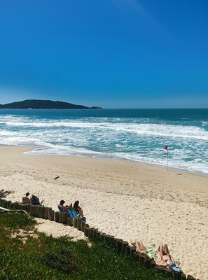 Una playa con una cerca de madera, gente relajándose y una bandera en la arena.