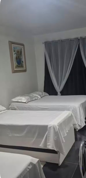 A room with two beds, a framed picture on the wall, and a curtain.