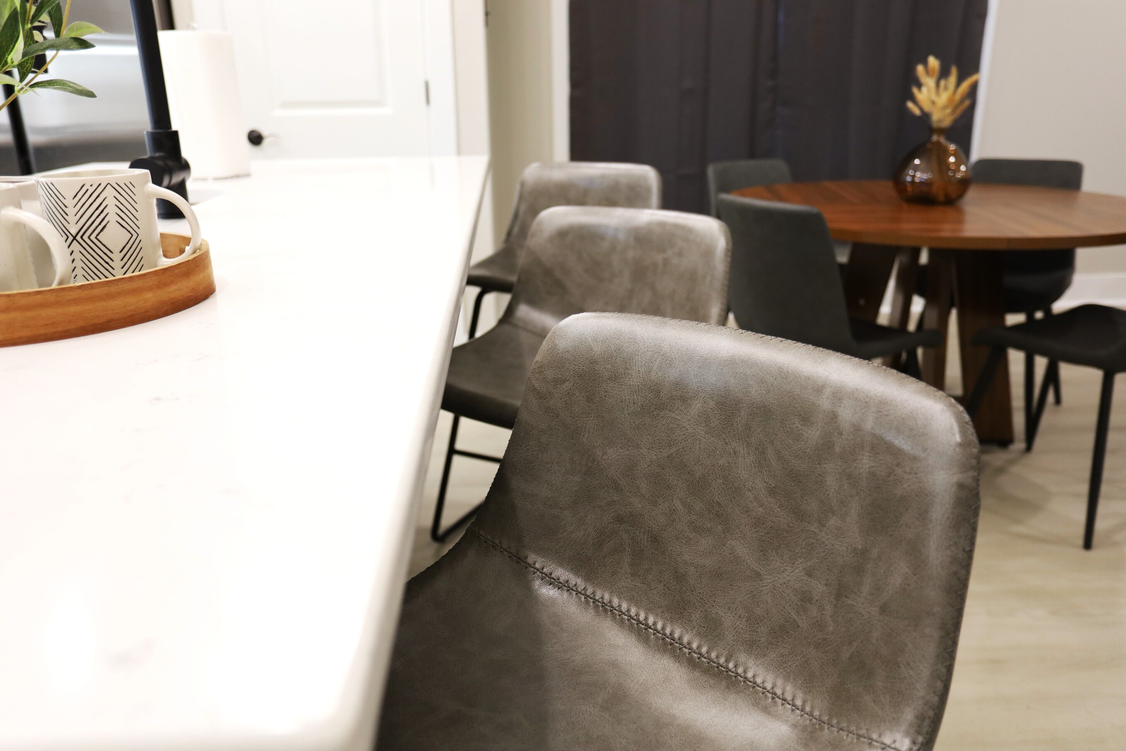 Een moderne eetruimte met een wit aanrechtblad, grijze bekleden stoelen en een houten tafel met een vaas.
