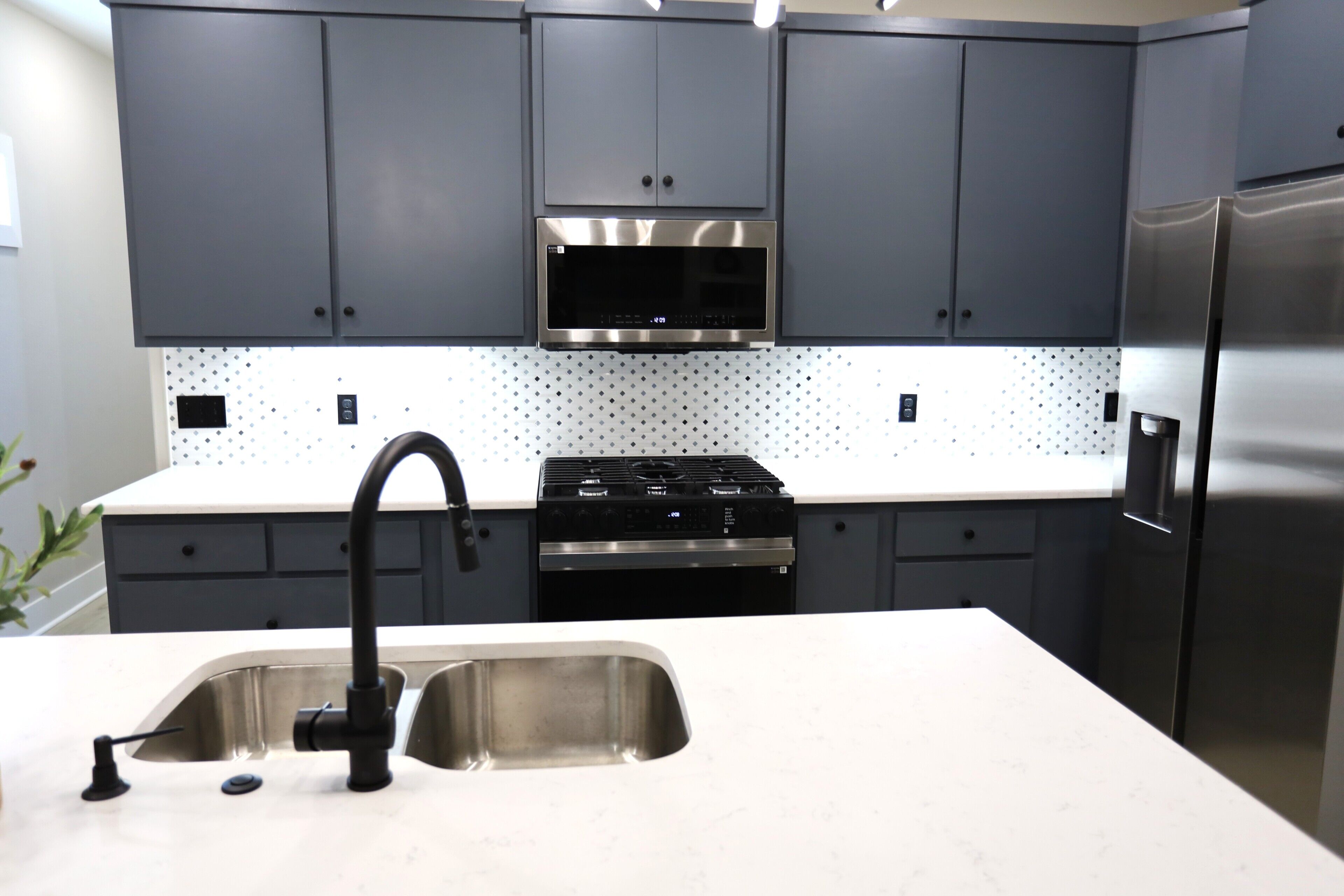 A modern kitchen with grey cabinets, a stainless steel refrigerator, a built-in oven, and a microwave.