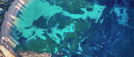 Vista aérea de una zona costera con playa, agua cristalina y un pequeño sector de vegetación.