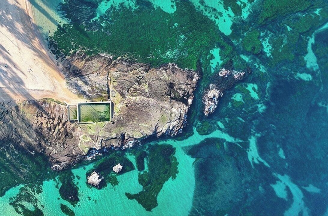 Vista aérea de una propiedad costera con costa rocosa, aguas turquesas cristalinas y una zona pequeña cercada.