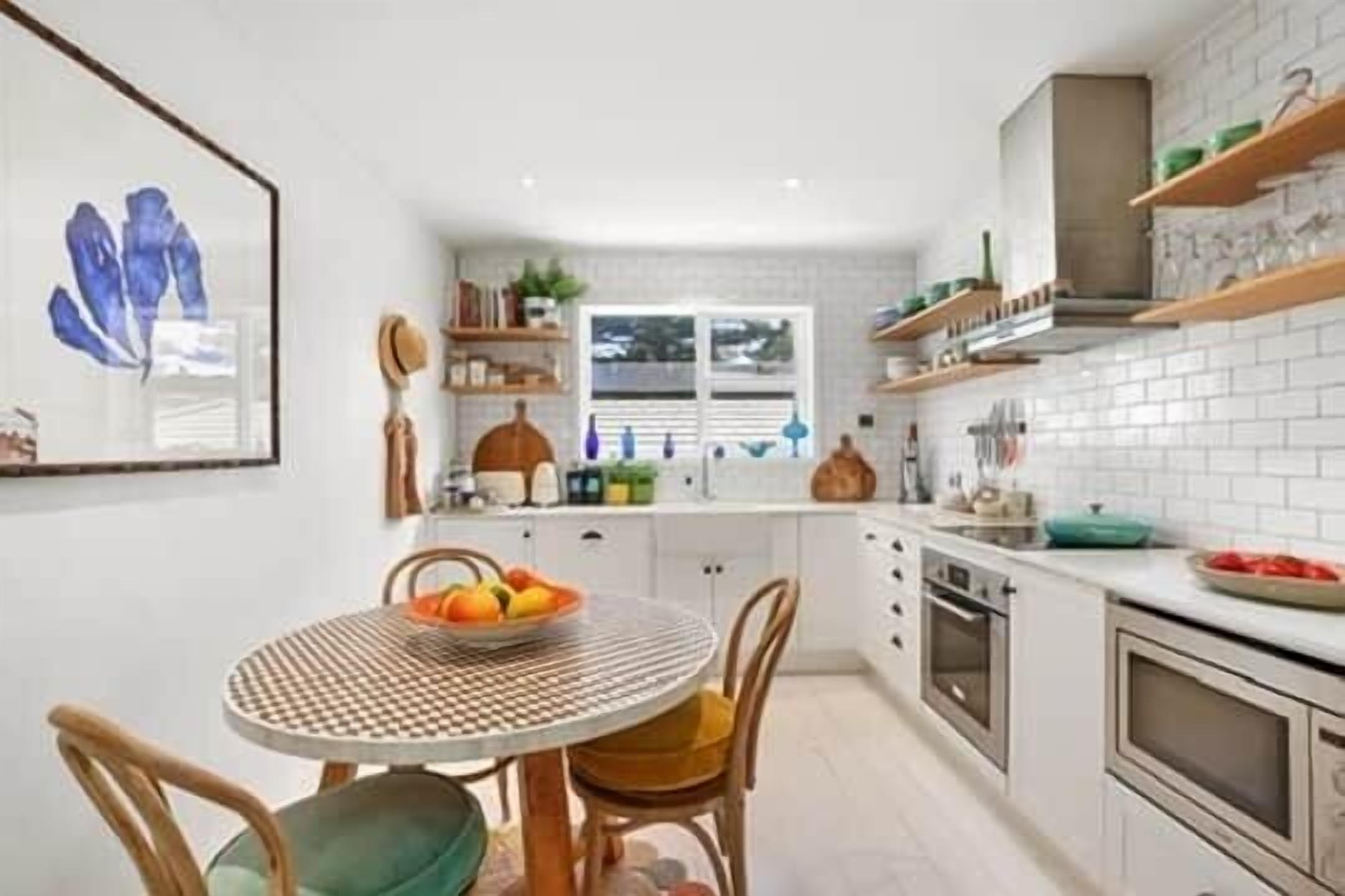Een moderne keuken met witte kastjes, een ronde eettafel met stoelen, en een raam dat natuurlijk licht binnenlaat.