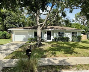 Une maison de plain-pied avec un garage, une pelouse devant et de grands arbres.