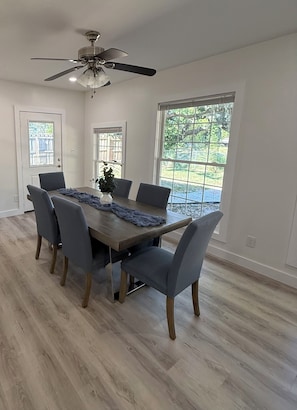 A dining area with a wooden table, six chairs, a ceiling fan, and large windows. - Peace in the City - clean, beautiful 3 BR - private backyard - and near beaches (Sarasota)