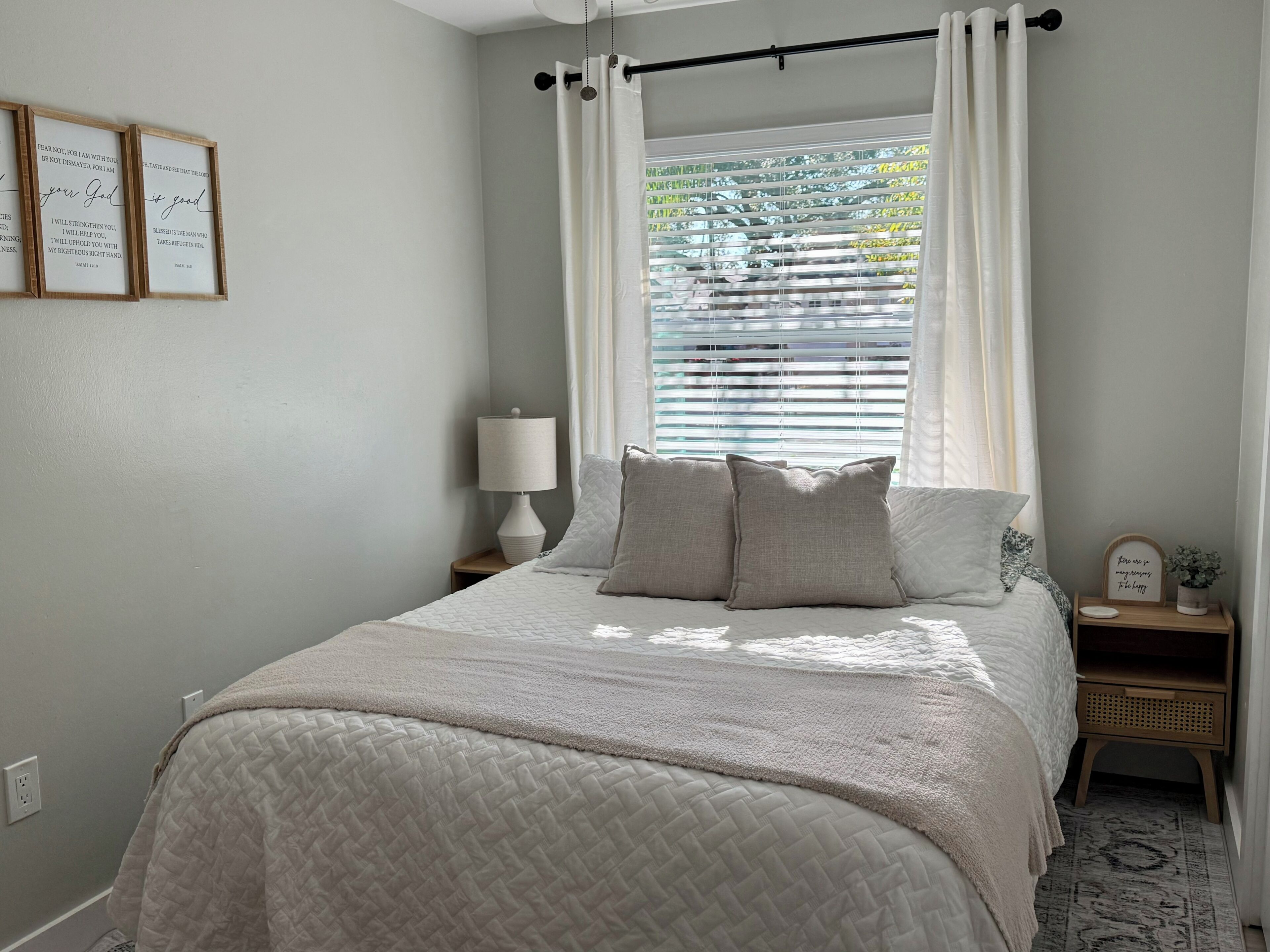 A bedroom with a bed, a nightstand, a lamp, and a window with blinds.