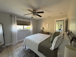 A bedroom with a bed, a nightstand, a ceiling fan, a window with curtains, and a mirror on the wall. - Peace in the City - clean, beautiful 3 BR - private backyard - and near beaches (Sarasota)