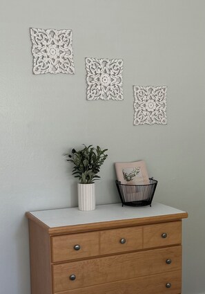 Une commode en bois avec des tiroirs, un vase blanc contenant des plantes vertes et une chaise noire avec un coussin.