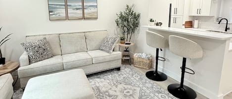 A modern living room with a sofa, ottoman, and a patterned rug.
