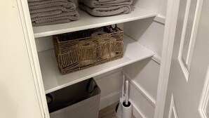 Ein Schrank mit Regalen, voll mit gefalteten Handtüchern und einem Korbwäschesammler.