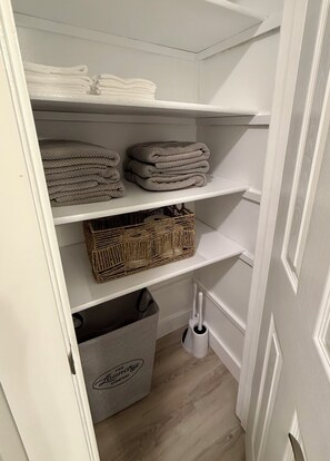 Ein Schrank mit Regalen, voll mit gefalteten Handtüchern und einem Korbwäschesammler.