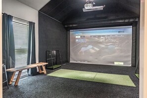 Ein Zimmer mit einer großen Projektionsleinwand, die ein Benutzerprofil zeigt, einer Holzbank, einem kleinen schwarzen Schrank und einer grünen Matte auf dem Boden.