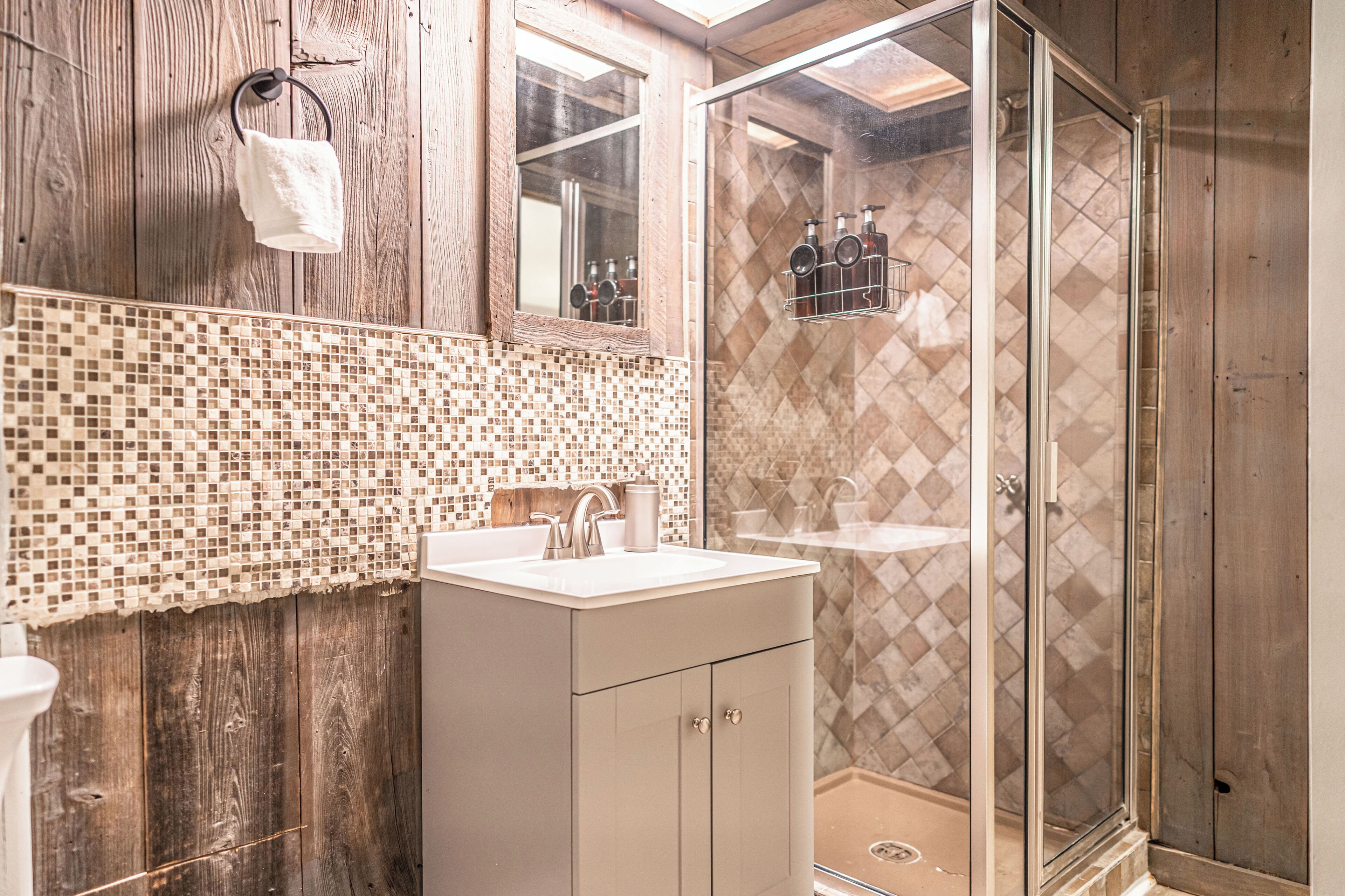 A bathroom with a wooden wall, a tiled backsplash, a sink, a mirror, and a shower area.