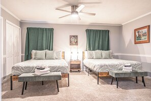 A bedroom with two beds, a nightstand, a bench, a ceiling fan, and a framed picture on the wall. - The Tipsy Hound - Golf Simulator! (Southern Pines)
