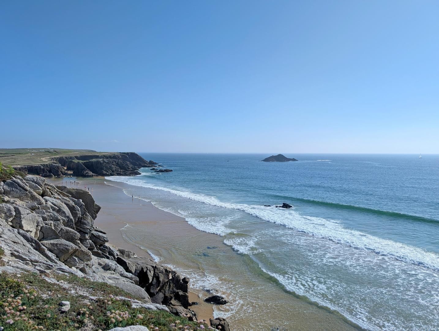 A coastal landscape with a rocky beach, clear blue sky, and calm sea.
