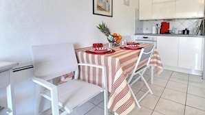 Ein Essbereich mit gestreiftem Tischlein, weißen Stühlen und einer Küche im Hintergrund.