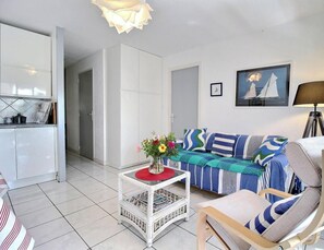 Ein modernes Wohnzimmer mit einer Couch, einem Sessel, einem Couchtisch mit Blumen und einem Bilderrahmen an der Wand, sowie einer Lampe.