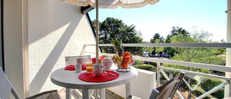 A balcony with a table set for breakfast, including a fruit bowl, a teapot, and a pitcher.