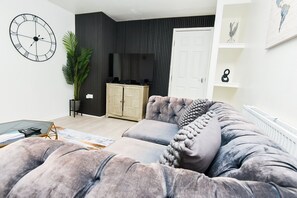 A modern living room with a tufted sofa, a large wall clock, a cabinet, and a potted plant.
