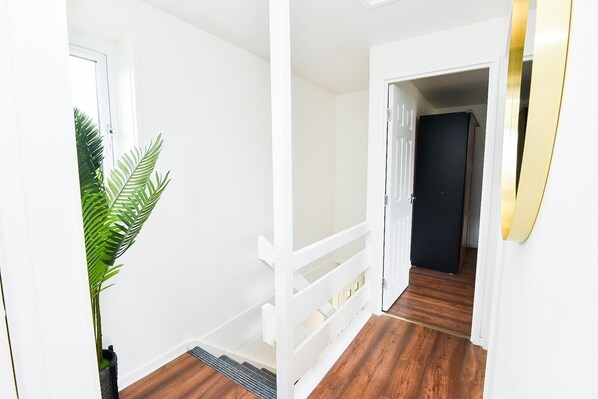 A hallway with white walls, a wooden floor, and a white railing.