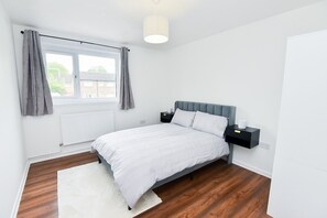 Ein Schlafzimmer mit einem Bett, Nachttischen, einem fensterbelaubten Fenster, einer Heizung und einer weißen Wand.
