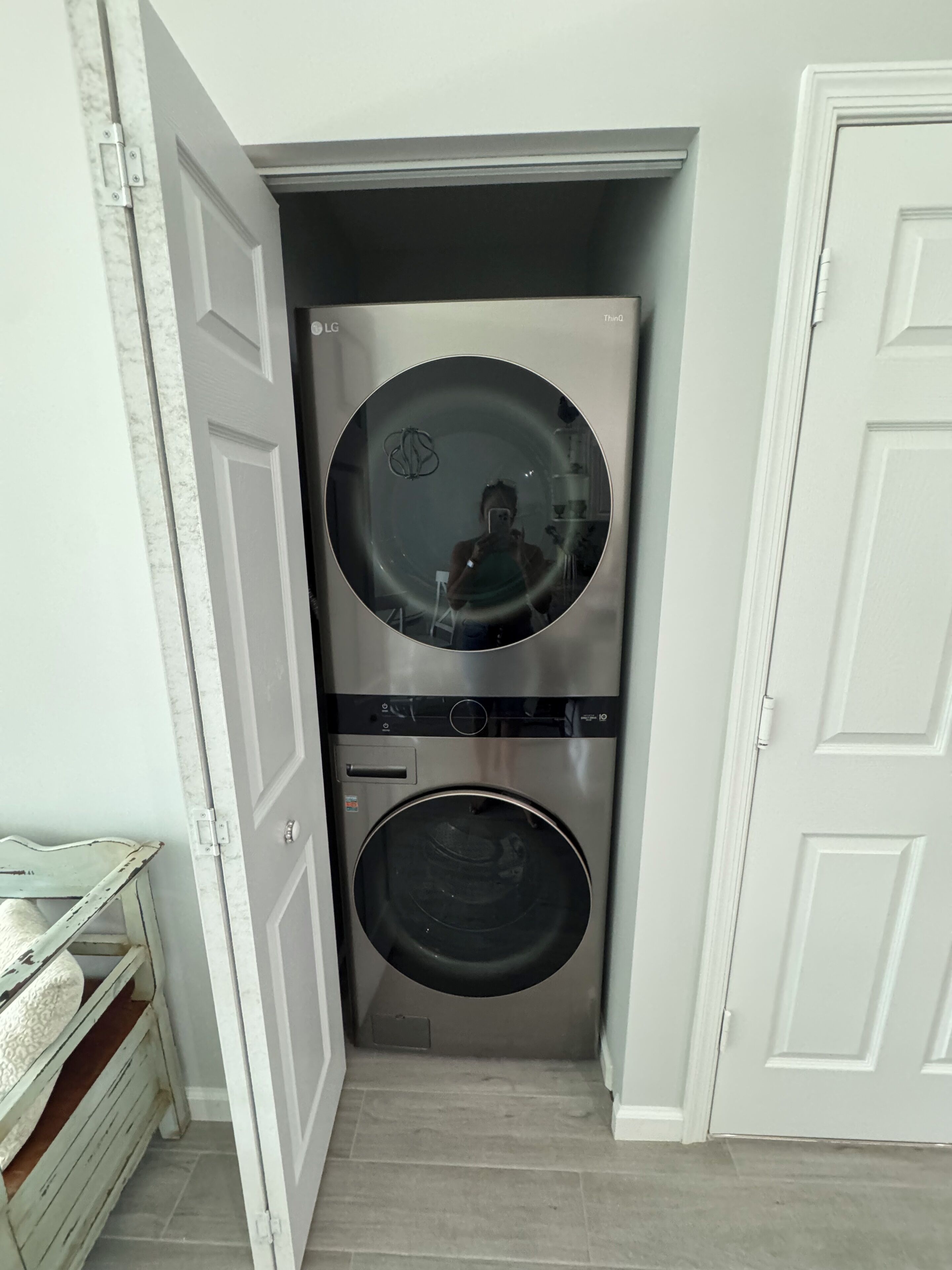 A compact laundry room with two stacked washing machines, a mirror, and a small shelf.