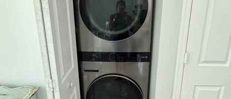 A compact laundry room with two stacked washing machines, a mirror, and a small shelf.