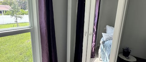 A bedroom with a large wardrobe, a window with curtains, and a view of the outdoors.