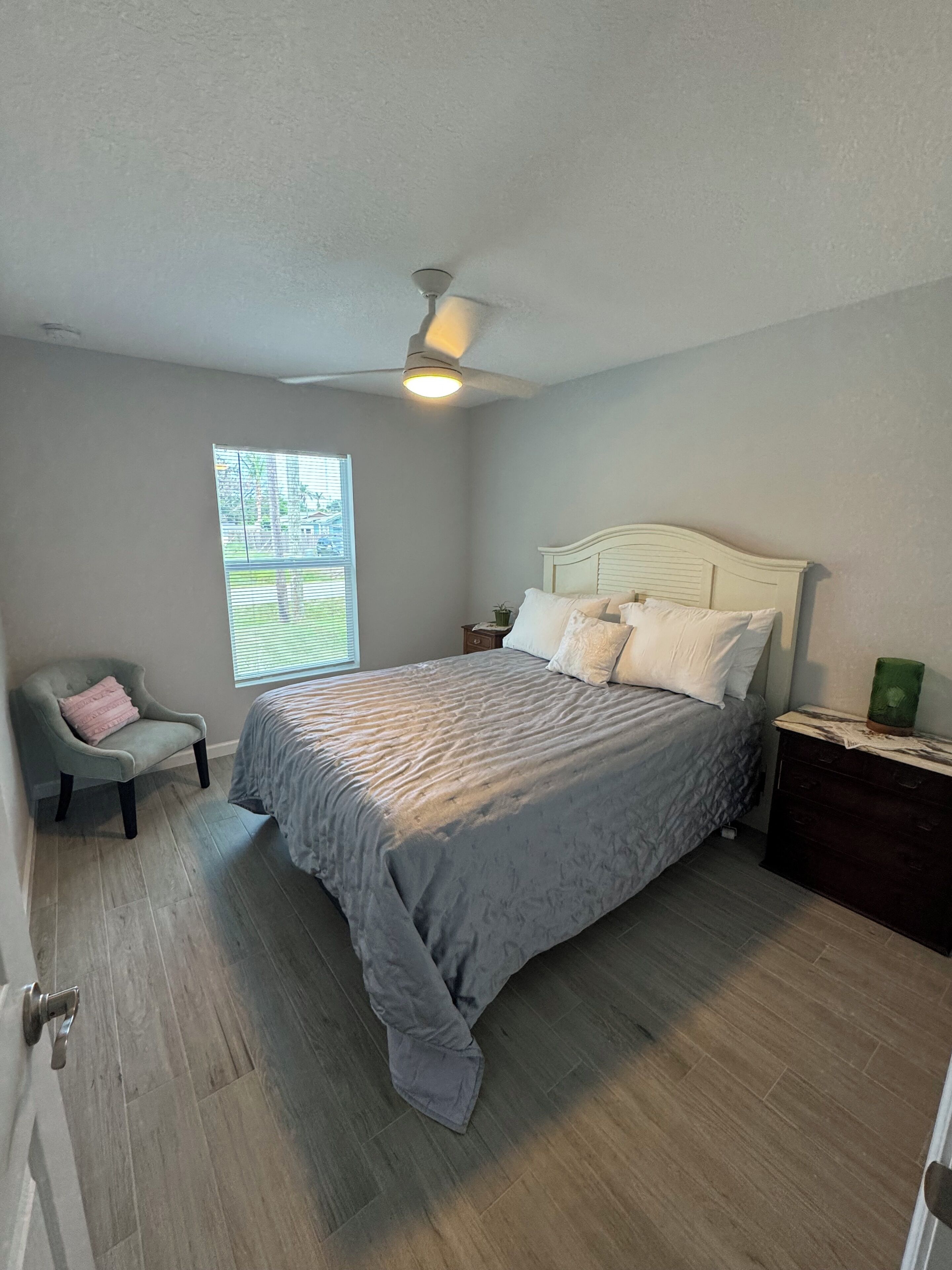 A bedroom with a bed, a chair, a nightstand, and a window.