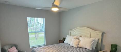 A bedroom with a bed, a chair, a nightstand, and a window.