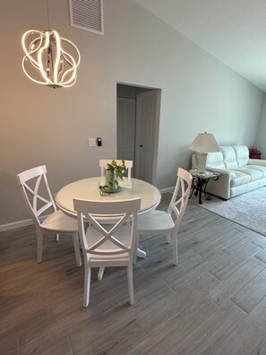A modern living space with a round dining table, white chairs, a white sofa, and a lamp. - The Normandy House -New Modern 3 Bedrooms 2 Bathroom retreat in Stuart (Stuart)