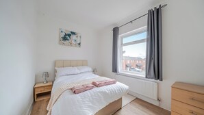 A bedroom with a bed, a nightstand, a dresser, a window with curtains, and a radiator.