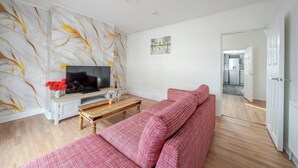 A living room with a TV, sofa, and a wall with a tree pattern.