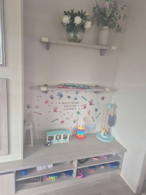 A child's room with a wall decorated with handprints and a motivational quote, a shelf with toys, and a small desk area.