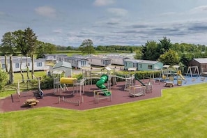 A playground with various play structures, including a green slide, in front of mobile homes.
