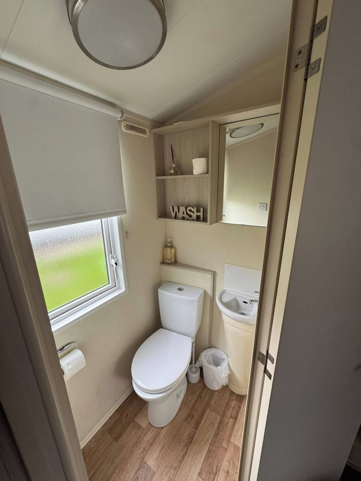 Une petite salle de bain comprenant des toilettes, un lavabo, un miroir et une étagère avec des articles de toilette.