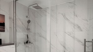 Une salle de bain moderne avec une douche à parois de verre, des murs en marbre et un lavabo blanc.