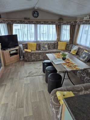 Ein Wohnzimmer mit Sofa, Poufs, einem Tisch mit Pflanze, einem Fernseher und einer Uhr an der Wand.