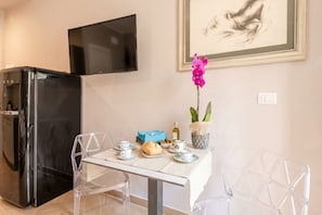 A modern kitchen with a black refrigerator, a dining table with chairs, and a television mounted on the wall. - 4-Bedroom, 4-Bathroom Elegant Residence with Balcony (Bari)