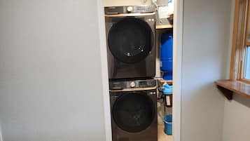 A laundry room with two stacked washers and dryers, a blue storage bin, and a wooden shelf.
