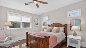 A bedroom with a wooden bed, a nightstand, a chair, a ceiling fan, and a window with blinds. - Downtown Rehoboth Beach House Quick Walk to Beach Pets Permitted (Rehoboth Beach)