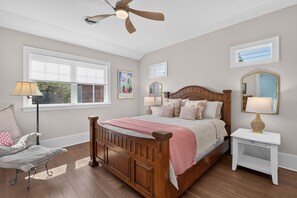 Ein Schlafzimmer mit einem hölzernen Bett, einem Nachttisch, einem Stuhl, einem Deckenventilator und einem Fenster mit Jalousien.
