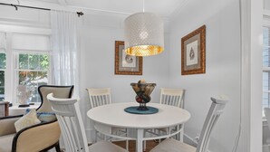 A round dining table with white chairs, a hanging light fixture, and framed artwork on the wall. - Downtown Rehoboth Beach House Quick Walk to Beach Pets Permitted (Rehoboth Beach)